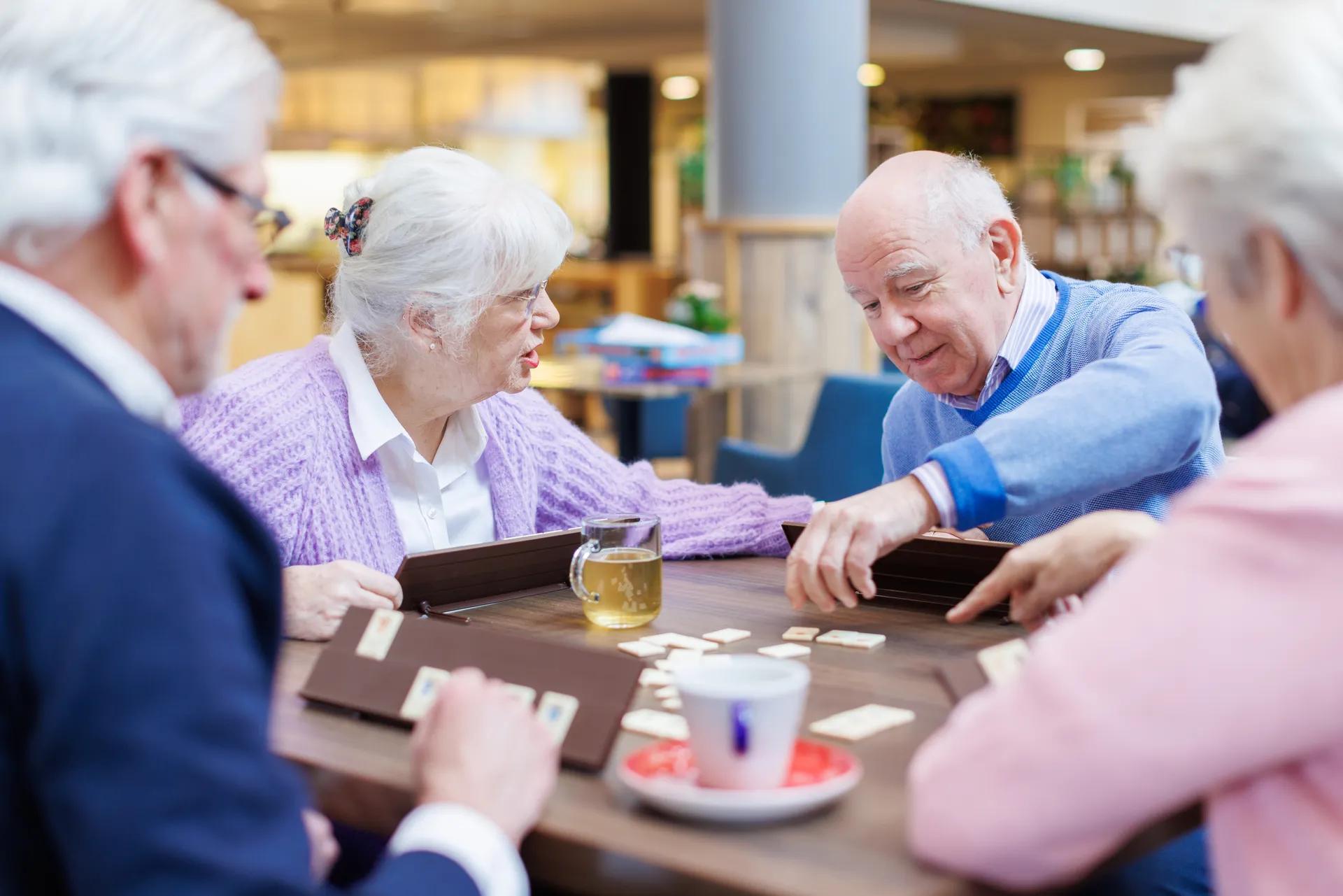 Vier ouderen aan tafel die rummikub aan het spelen zijn