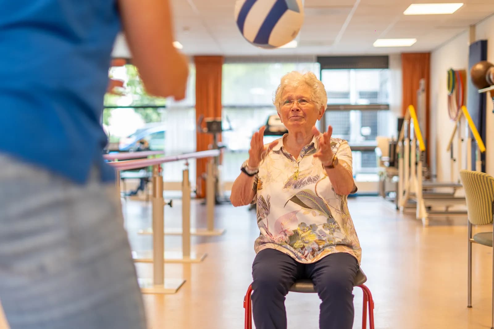 Mevrouw gooit een bal over met een fysiotherapeut als oefening.
