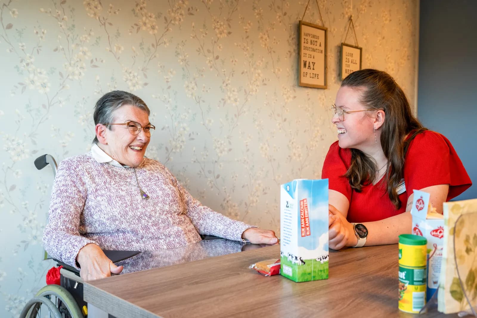 een oudere en een zorgmedewerker zitten aan tafel